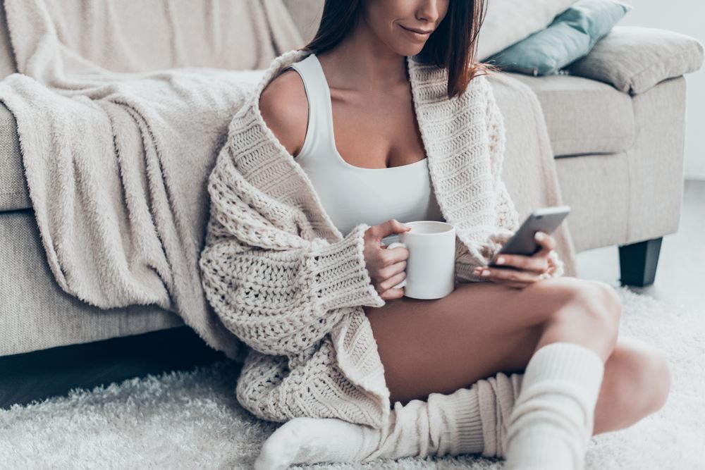 Sexy lady uses smart phone while sitting on carpet at home